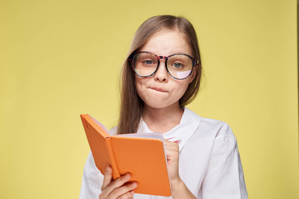 schoolgirl with textbook in hands learning childhood yellow background - Foto, Bild