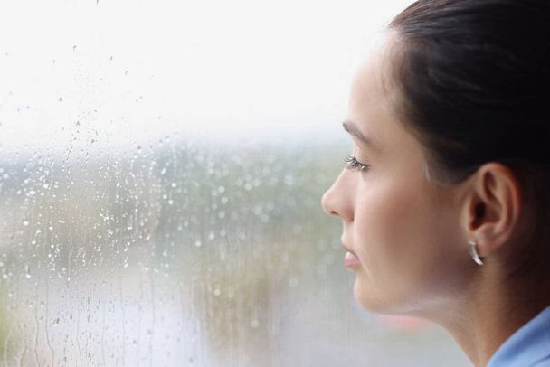 Young pensive woman looking out window at rain - Foto, afbeelding