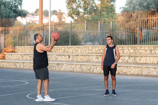 Баскетбольный тренер держит мяч. Счастливый подросток, играющий со старшим дедушкой. - Фото, изображение