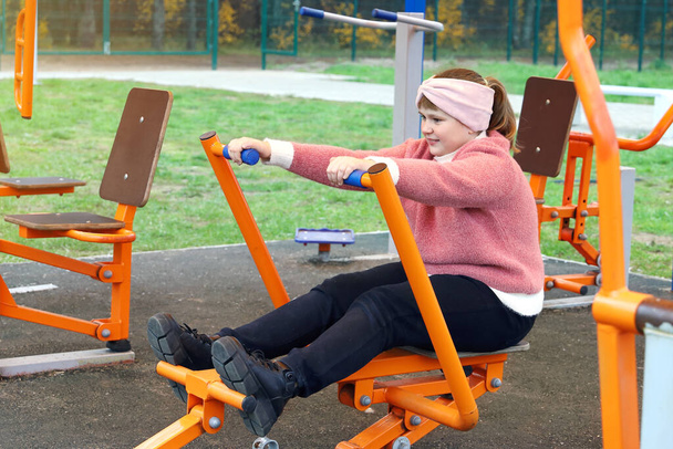 Chubby chica realiza ejercicios deportivos en simuladores de calle al aire libre - Foto, Imagen