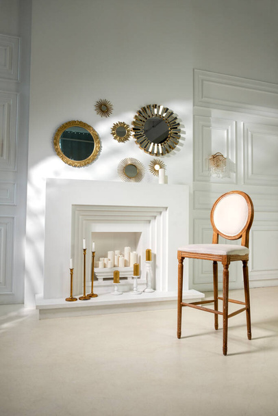 vintage fa szék a háttérben egy kandalló egy fehér fal nagy gyertyák és kerek arany tükrök - Fotó, kép