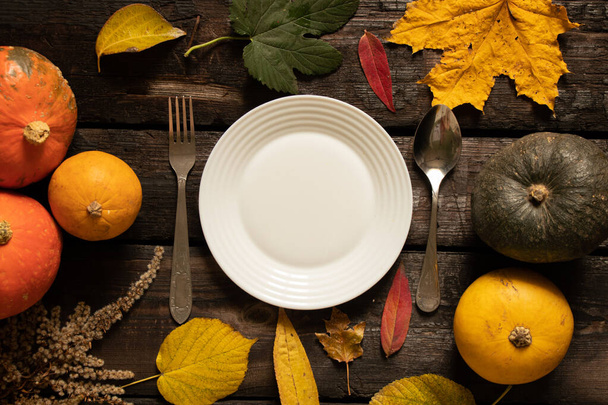 weißer Teller steht auf einem Holztisch neben Kürbissen und Herbstblättern, festliche herbstliche Tischdekoration, Teller auf dem Tisch - Foto, Bild