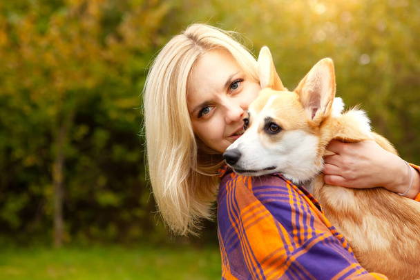 Portrait of a woman with a welsh corgi dog. Beautiful blonde woman with her beloved pet, looking at the camera. Natural autumn background. The concept of an active lifestyle with a pet. - Foto, Imagen