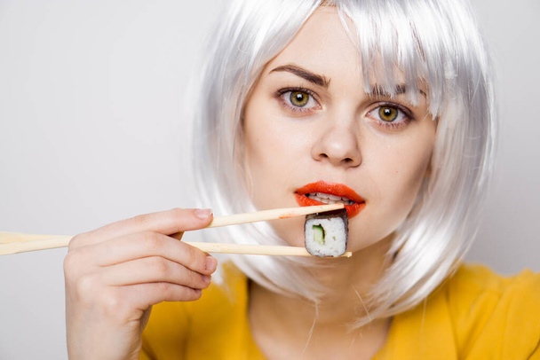 bonita mujer en peluca blanca y sushi con palillos japoneses - Foto, Imagen