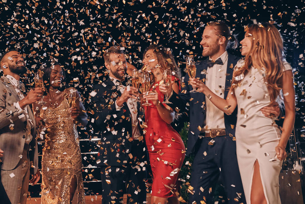 Group of beautiful people in formalwear having fun together with confetti flying all around - Photo, image