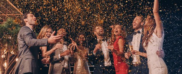 Group of happy people in formalwear having fun together with confetti flying all around - Zdjęcie, obraz