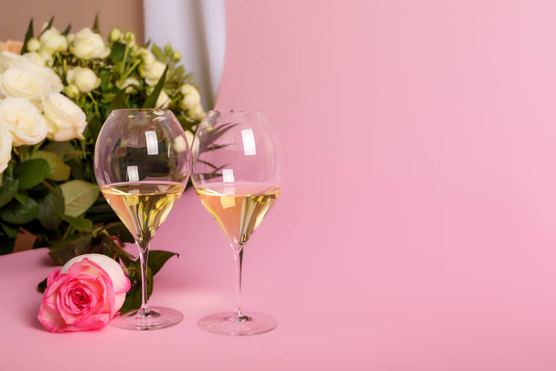 Beautiful roses and two glasses of white dry wine on pink background. Romantic composition with flowers and wine for Valentine's Day or romantic love dinner. Wedding card with flowers and wine glasses. Romantic mood and atmosphere. French white wine. - Photo, image