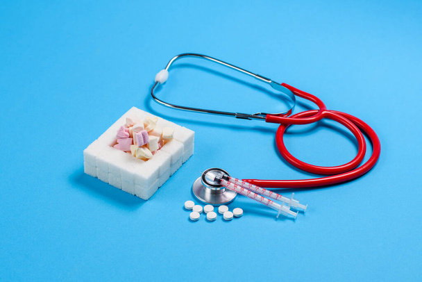 Свитки и сахар на синем фоне рядом с медицинскими инструментами. Концепция развития диабета от частого потребления сахара и сладостей - Фото, изображение