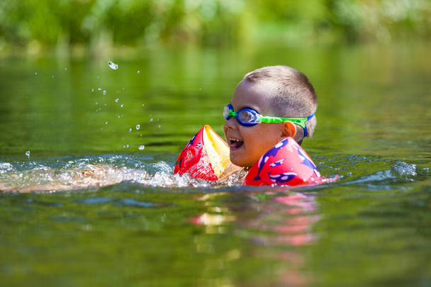 Leuke jongen zwemt in het riviertje met zijn armbanden en bril - Foto, afbeelding