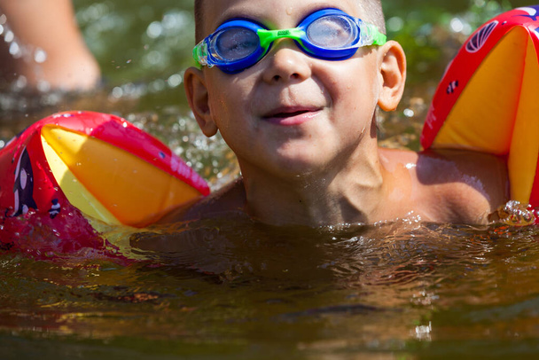 Leuke jongen zwemt in het riviertje met zijn armbanden en bril - Foto, afbeelding