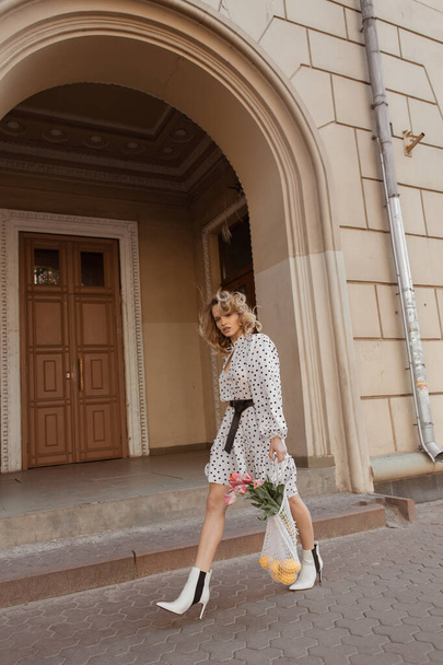 Street portrait of a stylish girl with flowers in a dress with blonde hair - Photo, Image