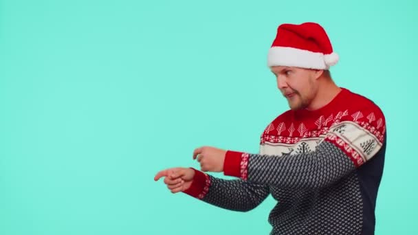Man wears red New Year sweater deer showing thumbs up and pointing at on blank advertisement space - Footage, Video