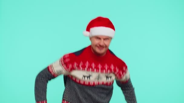 Hullu mies villapaidassa Joulupukin jouluhattu osoittaa kielensä ulos, pelleillä ympäriinsä tekemässä typeriä kasvoja - Materiaali, video
