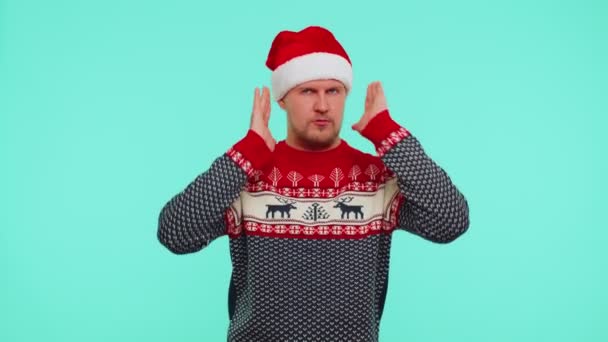 Uomo in maglione di Natale coprendo le orecchie e gesticolando no, evitando consigli ignorando il rumore sgradevole - Filmati, video