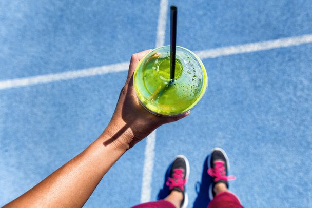 Gezonde detox groene smoothie cup food selfie pov toont running track en runner meisje met schoenen klaar om te lopen. Vierkante sociale media instagram gewas. - Foto, afbeelding