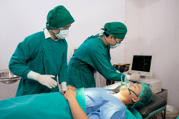 Zespół lekarz i asystent przygotowanie operacji i maska tlenowa z nagłym wypadkiem pacjenta w sali operacyjnej w szpitalu, chirurgii gojenia i chirurgii z monitorem patrzenia, problem z oddychaniem. - Zdjęcie, obraz