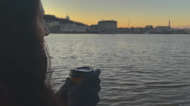 Dame boire du café chaud près de la rivière dans la ville dans la soirée - Séquence, vidéo