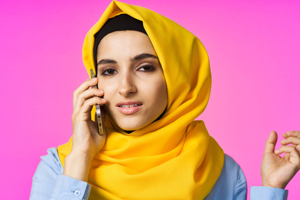 muslim woman in yellow hijab talking on the phone pink technology background - Fotografie, Obrázek