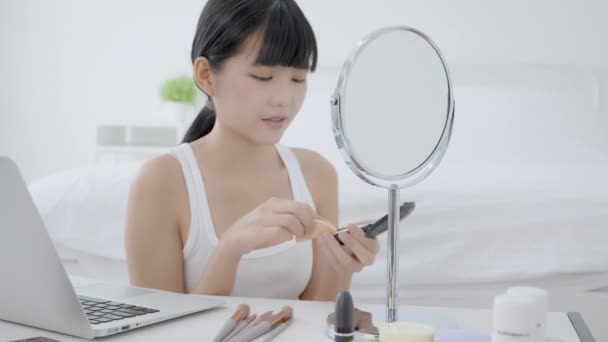 Yanağında pudra pudrasıyla makyaj yapmayı öğrenen genç Asyalı bir kadın özel ders veren bir dizüstü bilgisayar izliyor ve canlı yayında makyaj malzemeleriyle makyaj yapıyor.. - Video, Çekim