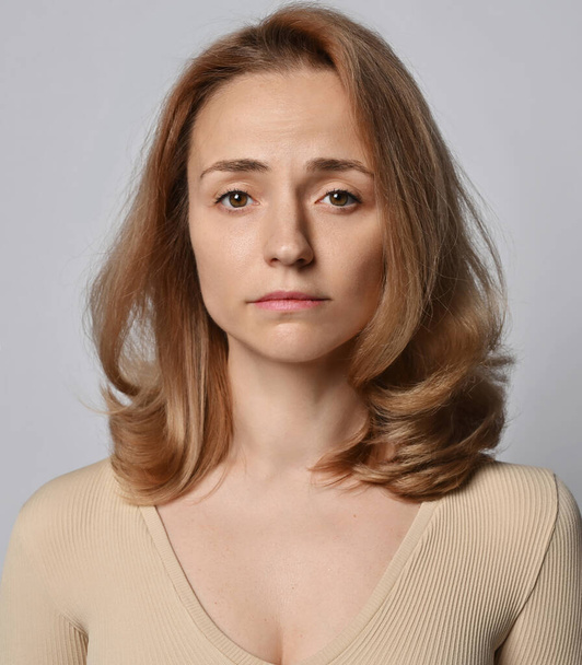Portrait of young blonde woman in beige shirt with long sleeves looking at camera with no smiling - Фото, изображение