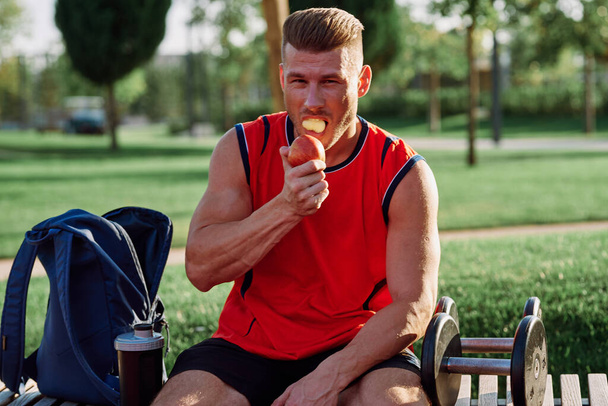 sporty man resting in the park on a bench having a snack - Zdjęcie, obraz