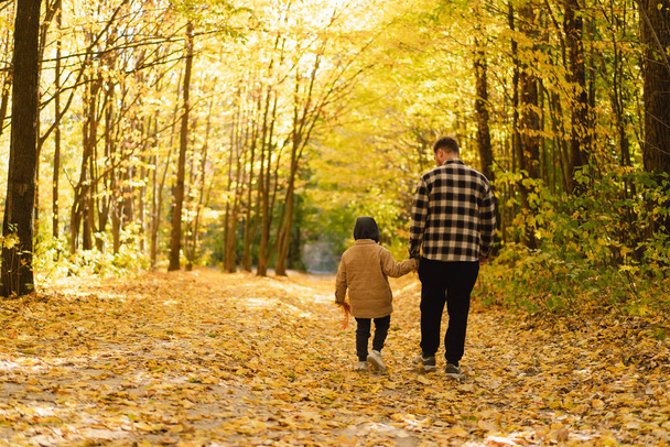 Happy dad and son are walking in the autumn forest. Autumn outdoor activity for family with kids. - Foto, imagen