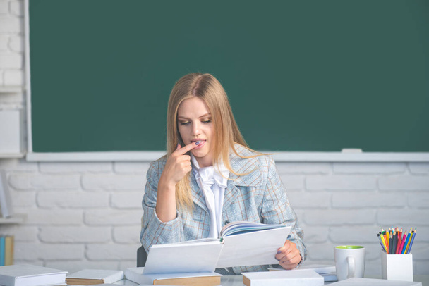 Female college student holding book in classroom, preparing for exam. Female student reading book on blackboard background with copy space. - Valokuva, kuva