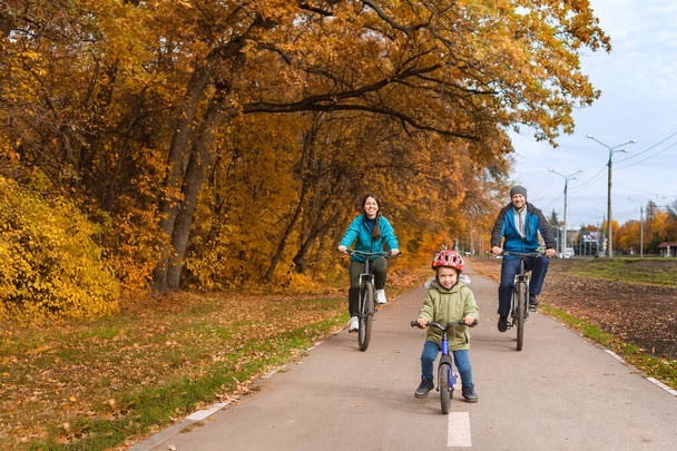 family with child riding on bikes together in autumn park - Photo, image