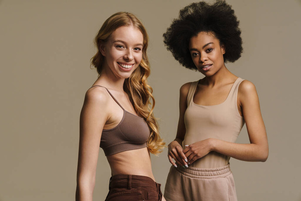 Two diverse young women in underwear standing over beige background - Foto, afbeelding