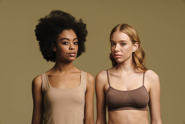 Two diverse young women in underwear standing over beige background - Foto, Bild