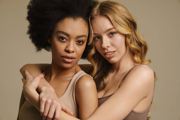 Two diverse young women in underwear standing over beige background close up - Fotó, kép