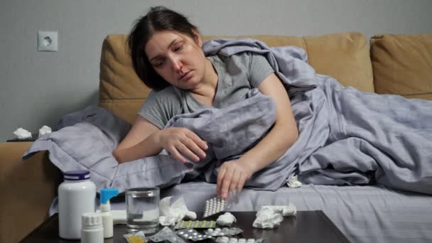 Mujer enferma toma medicinas y bebe agua tumbada en el sofá - Metraje, vídeo