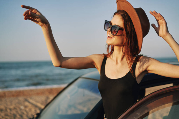cheerful woman in sunglasses and a hat on the ocean near the car - Photo, Image