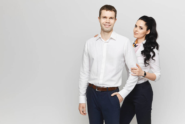 A pretty model girl in trendy office clothes and a young handsome man in formal clothes pose together on the grey background. Concept of friendship and partnership in business - Фото, зображення