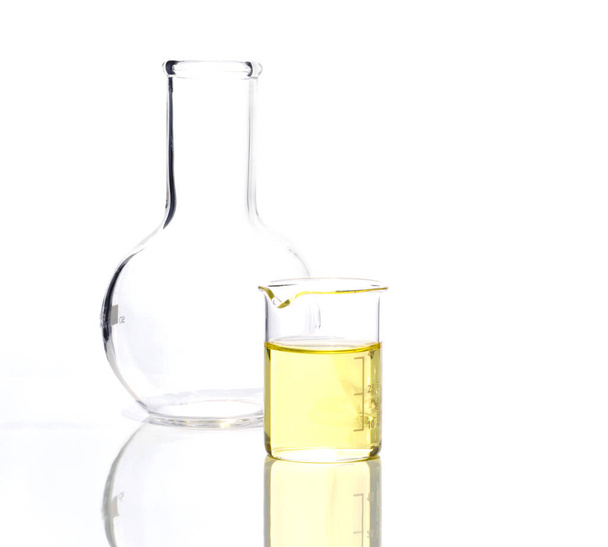 Ingrediente químico cosmético en mesa de laboratorio blanca. Poli líquido de cloruro de aluminio en el vaso de precipitados junto al matraz de fondo plano (vidrio de borosilicato). Vista lateral - Foto, imagen