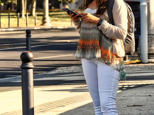 Žena v bílých kalhotách s mobilem čeká na semaforu - Fotografie, Obrázek