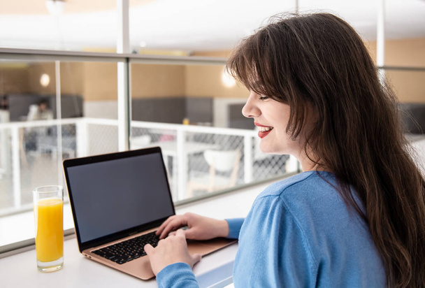 Aantrekkelijke jonge vrouw met een glas sap zit voor een laptop. - Foto, afbeelding