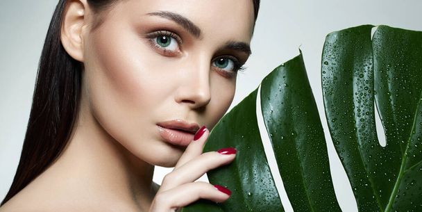 Beauty Portrait of brunette girl in palm leaves. Beautiful young woman with Make-up. Natural cosmetics concept - Photo, Image