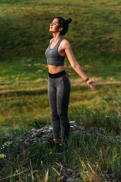A slender woman does yoga exercises against an incredible backdrop of nature. A woman does yoga in the open air. Healthy and yoga concept. Girl does gymnastics on fresh air in a hike on the nature. - Photo, image