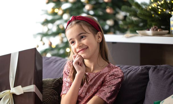 Милая маленькая девочка ждет Рождество дома на диване. - Фото, изображение
