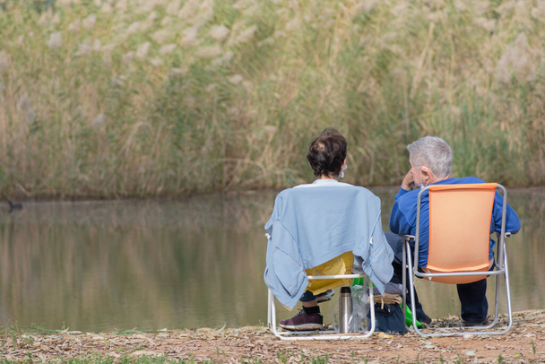 Uomo e donna seduti e rilassanti insieme all'aperto, di fronte all'acqua.  - Foto, immagini