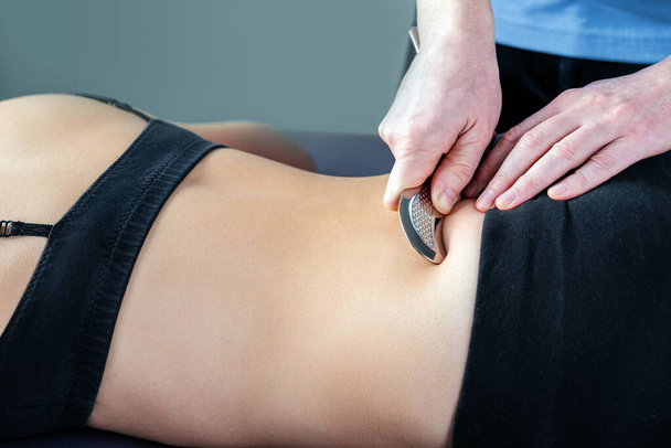 Фізіотерапевт фіксує біль у суглобах сакроліаку за допомогою методу IASTM. - Фото, зображення