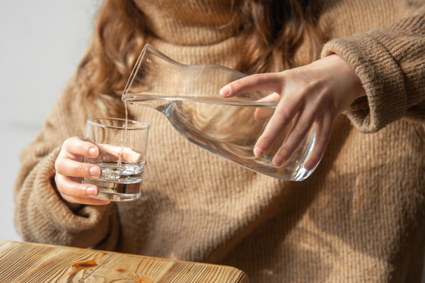 Eine Frau gießt Wasser aus einer Glaskaraffe in ein Glas. - Foto, Bild