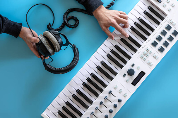 Чоловічі руки грають музичні клавіші і тримають навушники на синьому фоні, вид зверху
. - Фото, зображення