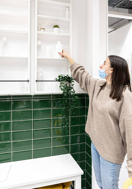 Mujer joven en un baño con azulejos verdes y armarios blancos en la pared. - Foto, imagen