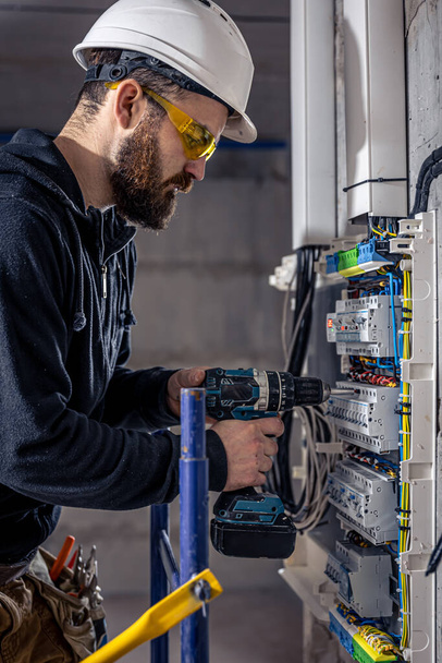 un electricista macho trabaja en una centralita con un cable de conexión eléctrico
. - Foto, Imagen