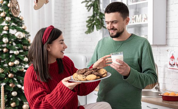Щасливий чоловік і дружина з різдвяним печивом і молоком на кухні
. - Фото, зображення
