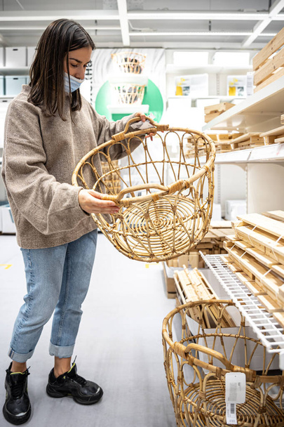 Young woman wearing a protective medical mask chooses a basket in a store. - Photo, Image
