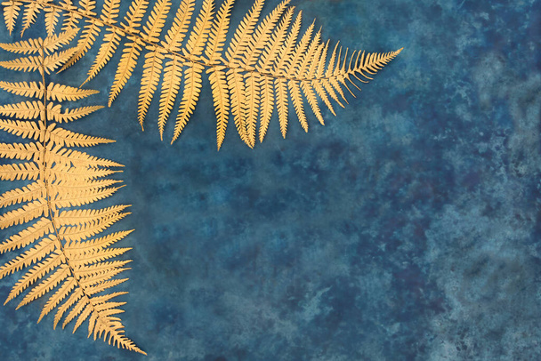 Gold fern leaf border on mottled blue background. Nature design concept. Top view, flat lay, copy space,  - Photo, Image