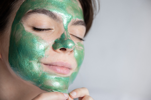 Aantrekkelijke jonge vrouw met een groen cosmetisch masker op haar gezicht, kopieer ruimte. - Foto, afbeelding